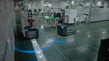 PUDU MP2000 carrying a pallet of cartons along a projected arrow path in an electronics factory, with a second unloaded MP2000 beside production equipment