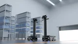 Two PUDU T150 delivery robots side by side on a warehouse floor beside grey shelving stocked with blue totes, with a roller door on the right
