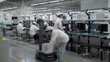 PUDU T300 Standard on an electronics assembly line, with a worker in cleanroom clothing loading stacks of white trays onto its deck