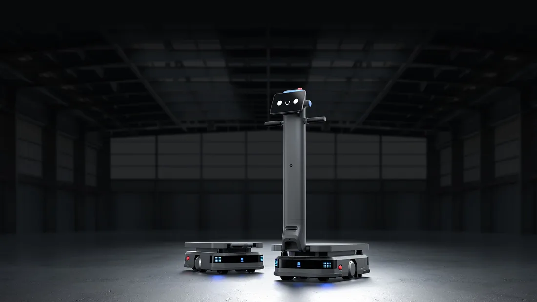 PUDU T600 Underride low-profile chassis robot beside the PUDU T600 Upright with its tall column, face display screen and handlebars, in a dark, empty warehouse